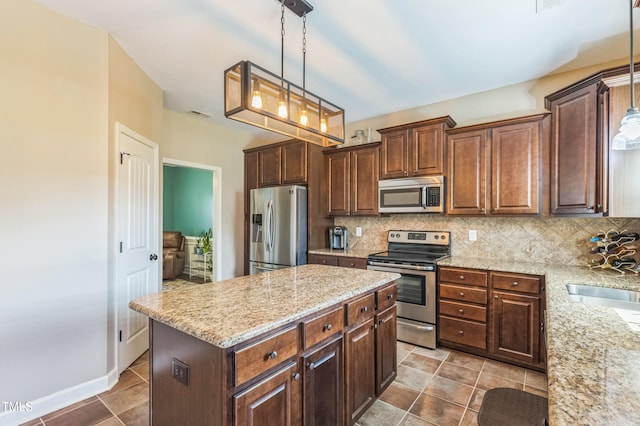 kitchen with backsplash, light stone countertops, a center island, and stainless steel appliances