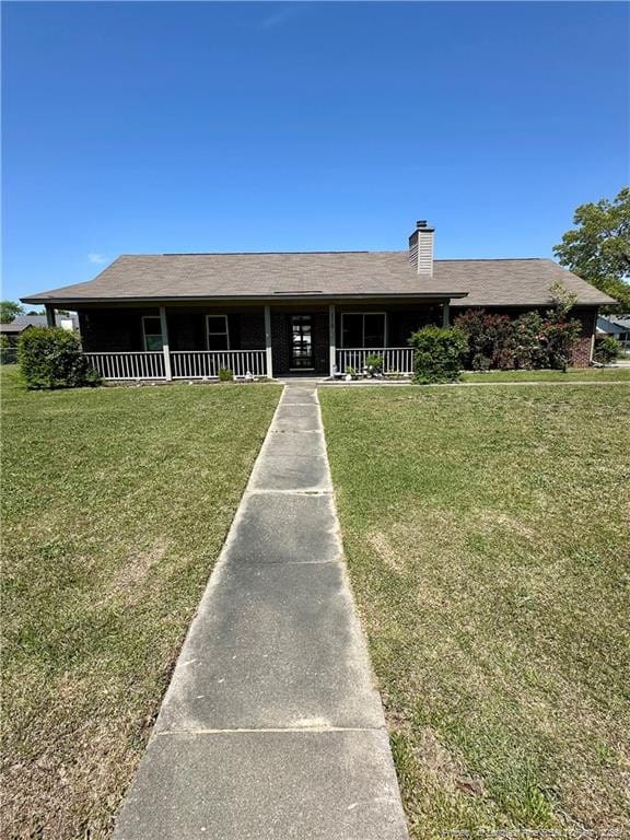 view of front of house featuring a chimney, a front lawn, and covered porch