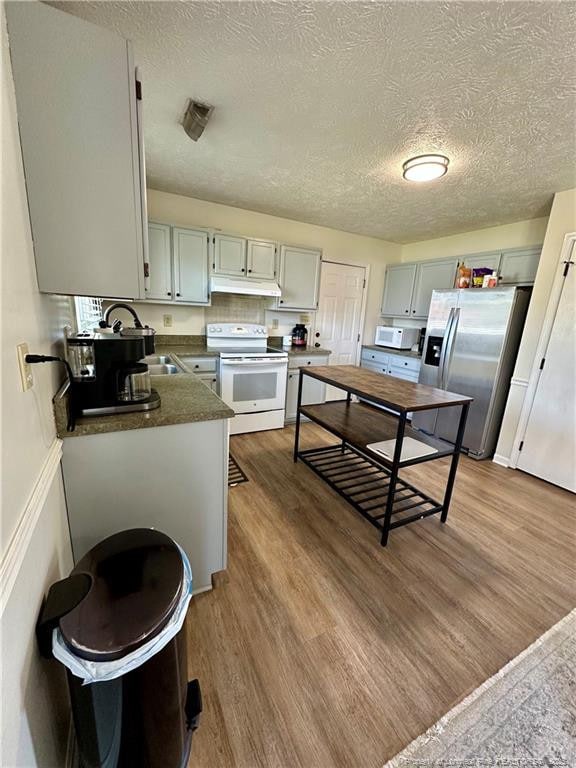 kitchen featuring under cabinet range hood, white appliances, a textured ceiling, and dark countertops