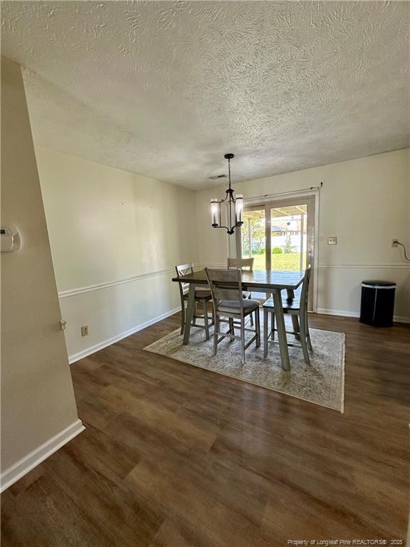 dining room with wood finished floors, a textured ceiling, baseboards, and a notable chandelier