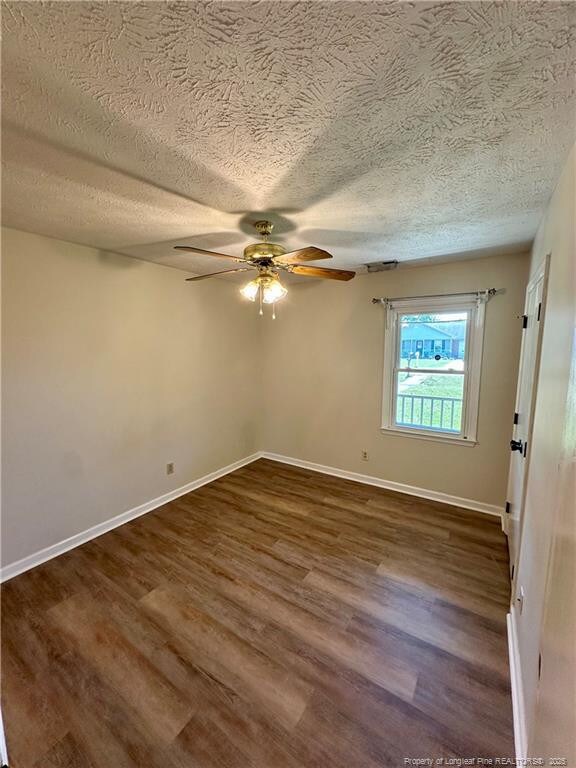 spare room featuring ceiling fan, a textured ceiling, baseboards, and dark wood-style flooring