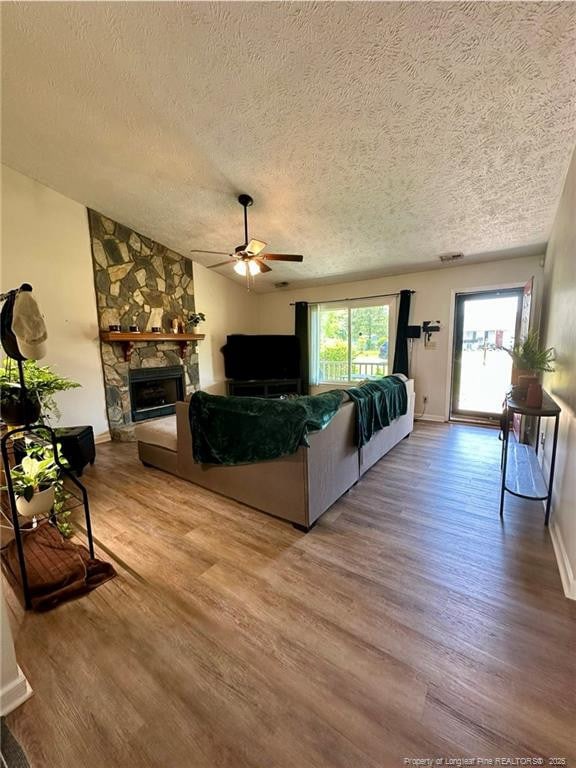 living area with a ceiling fan, wood finished floors, a textured ceiling, and a fireplace