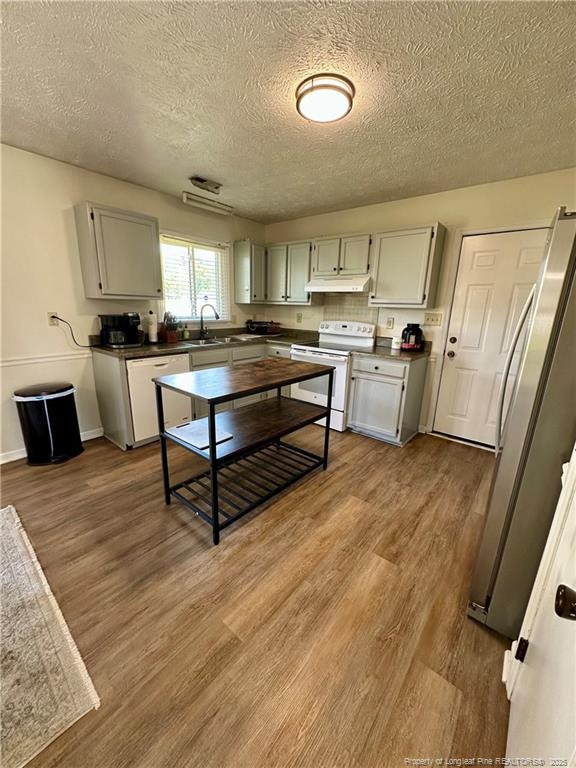 kitchen featuring a textured ceiling, baseboards, wood finished floors, white appliances, and under cabinet range hood