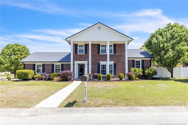 neoclassical home featuring brick siding, metal roof, and fence