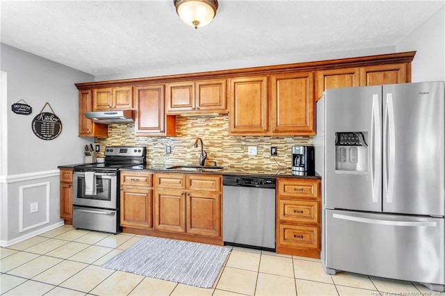 kitchen featuring brown cabinetry, appliances with stainless steel finishes, under cabinet range hood, and a sink