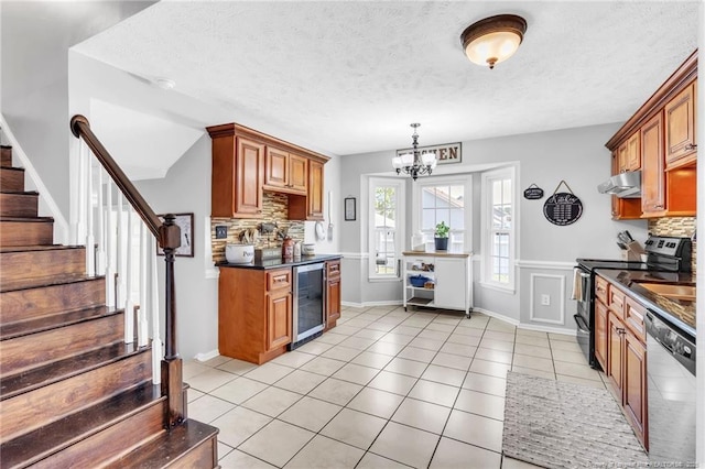 kitchen featuring beverage cooler, under cabinet range hood, dark countertops, tasteful backsplash, and appliances with stainless steel finishes