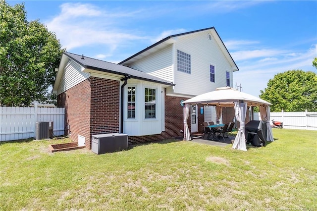 back of property featuring a fenced backyard, a yard, central AC, brick siding, and a gazebo