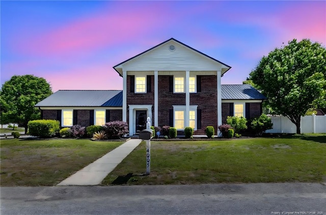 neoclassical / greek revival house with brick siding, fence, a yard, and metal roof