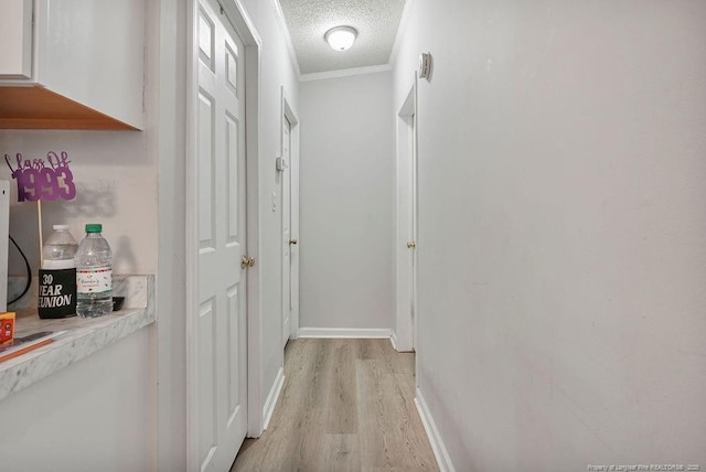 hall with light wood-type flooring, baseboards, a textured ceiling, and ornamental molding