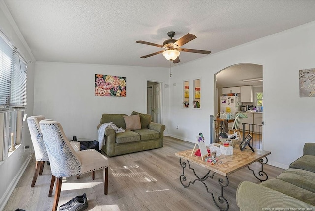 living area featuring arched walkways, baseboards, light wood-style flooring, a textured ceiling, and ceiling fan