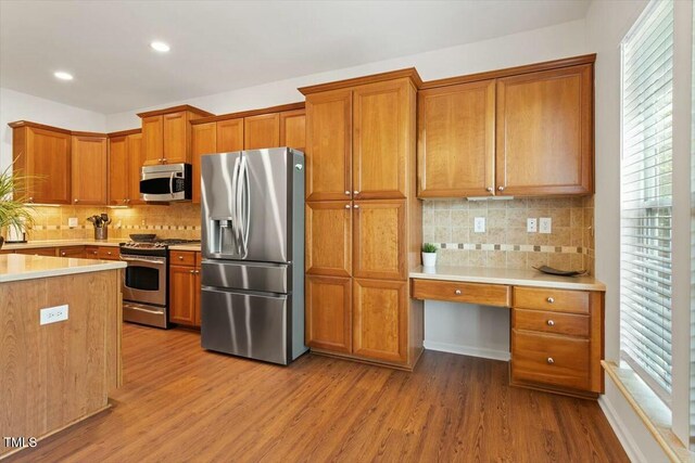803 Footbridge Pl, Cary, NC 27519 - kitchen featuring stainless steel appliances, built in desk, backsplash, wood finished floors, and brown cabinetry