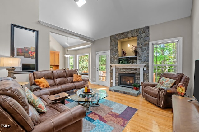 living room featuring a stone fireplace, light wood finished floors, and lofted ceiling