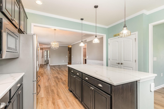 kitchen with a center island, light wood-style flooring, stainless steel microwave, crown molding, and hanging light fixtures
