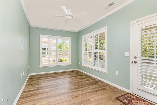 empty room featuring wood finished floors, ceiling fan, baseboards, ornamental molding, and visible vents