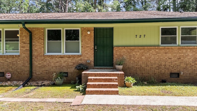 doorway to property featuring brick siding, crawl space, and roof with shingles