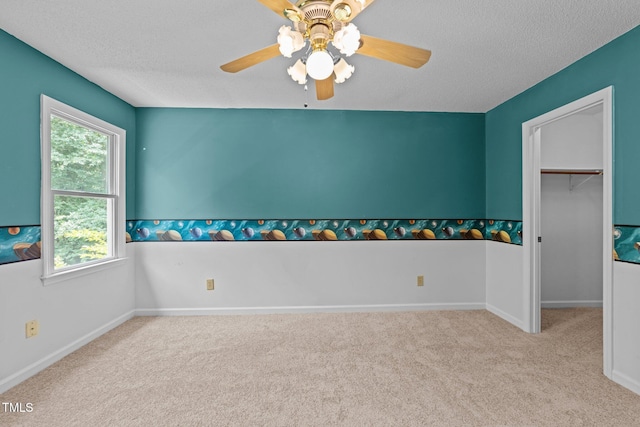 empty room featuring carpet floors, ceiling fan, a textured ceiling, and baseboards