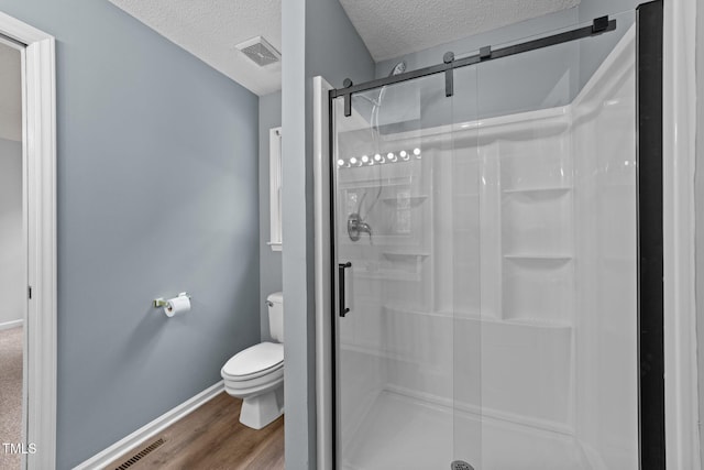 full bath featuring a textured ceiling, toilet, a shower stall, baseboards, and wood finished floors