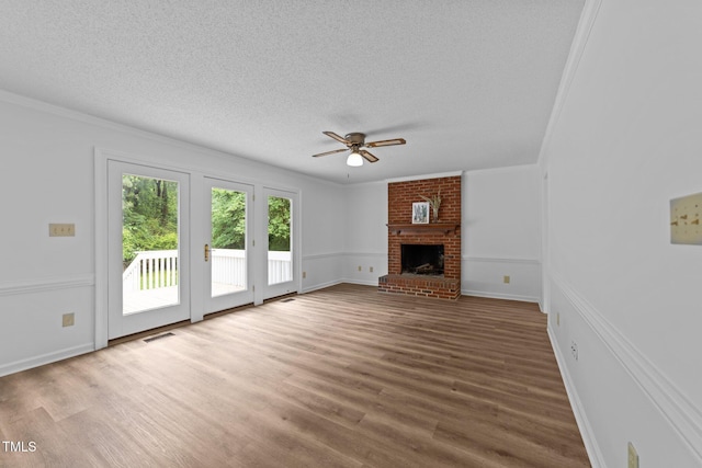 unfurnished living room featuring a ceiling fan, wood finished floors, a textured ceiling, a brick fireplace, and crown molding