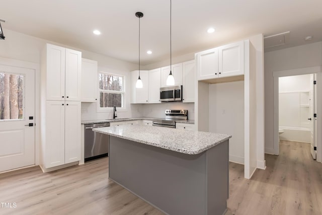 kitchen with a center island, stainless steel appliances, light wood finished floors, white cabinetry, and light stone countertops