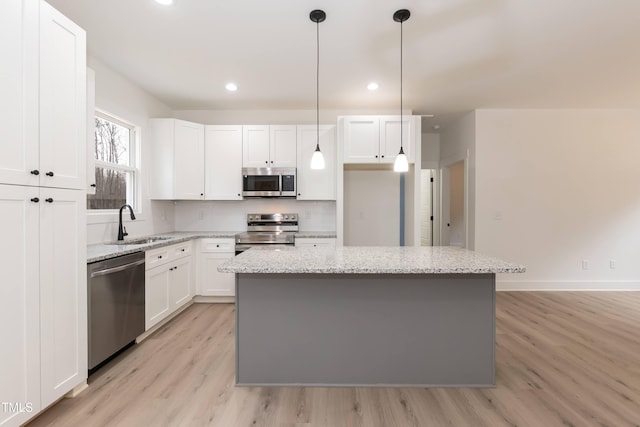 kitchen with light wood finished floors, stainless steel appliances, a center island, white cabinets, and a sink