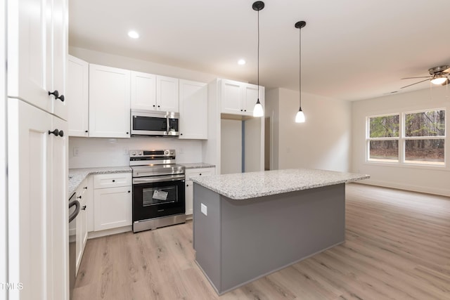 kitchen with light wood finished floors, white cabinets, pendant lighting, a kitchen island, and appliances with stainless steel finishes