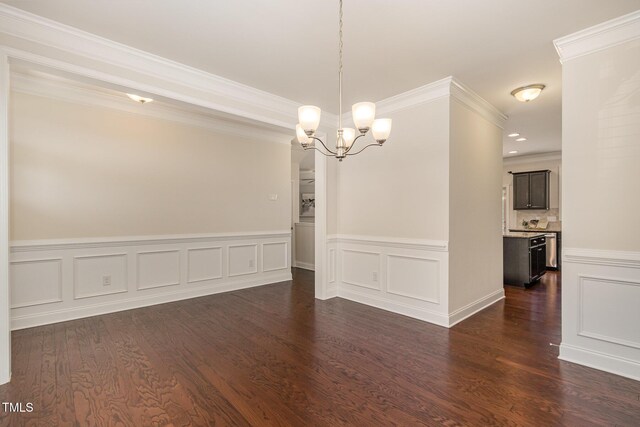 unfurnished dining area featuring wainscoting, a decorative wall, a chandelier, ornamental molding, and dark wood-style floors
