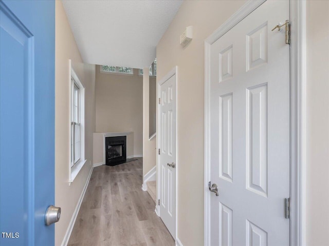 hallway featuring light wood-style floors, baseboards, and a textured ceiling