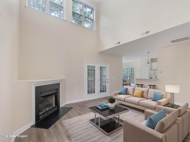 living area featuring light wood finished floors, a high ceiling, baseboards, and a fireplace