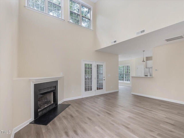 unfurnished living room with light wood-type flooring, a fireplace, a towering ceiling, and baseboards