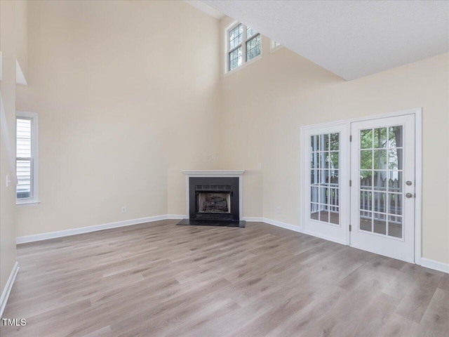 unfurnished living room featuring a high ceiling, wood finished floors, baseboards, and a fireplace with flush hearth