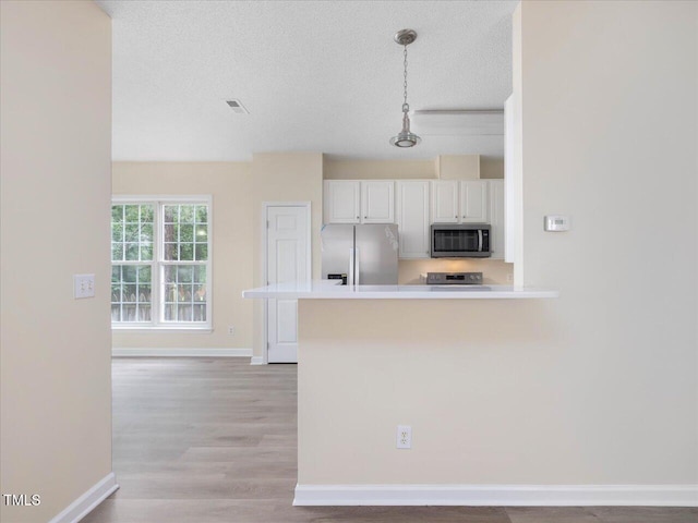 kitchen with stainless steel appliances, a textured ceiling, white cabinets, baseboards, and a peninsula