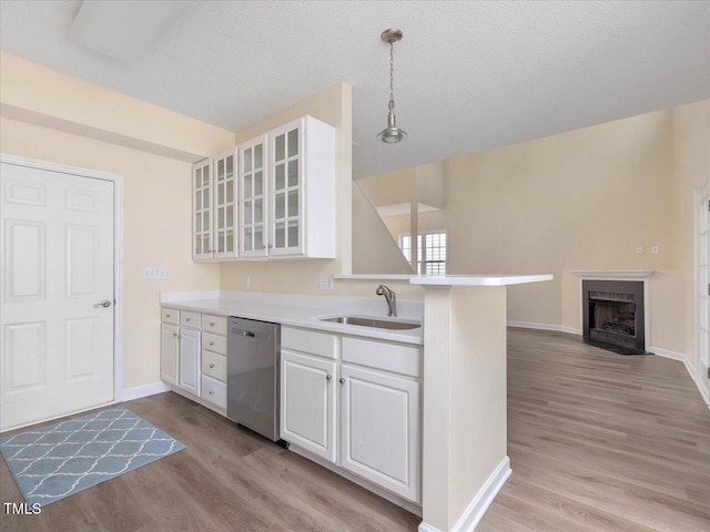 kitchen featuring stainless steel dishwasher, a sink, light wood finished floors, white cabinets, and a textured ceiling