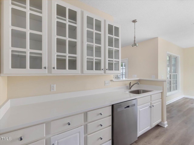 kitchen with stainless steel dishwasher, a sink, glass insert cabinets, white cabinetry, and light countertops