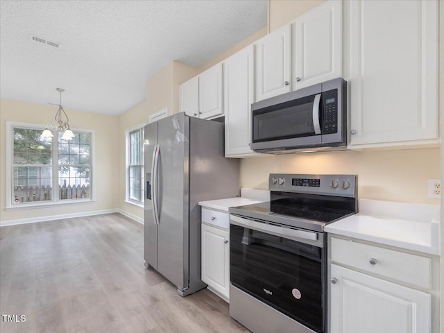 kitchen featuring appliances with stainless steel finishes, light wood-style flooring, white cabinets, light countertops, and a chandelier