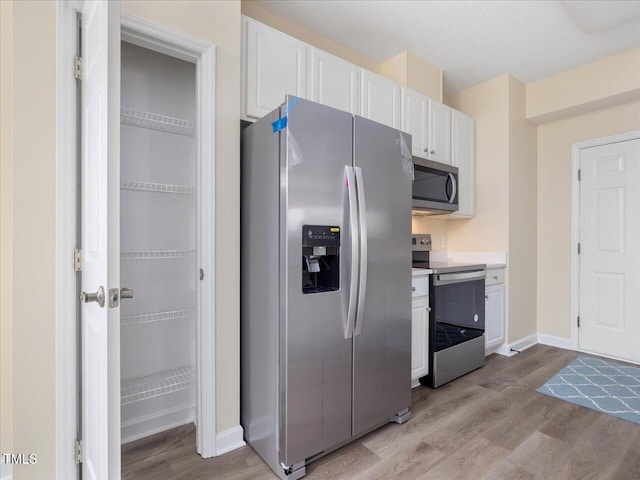 kitchen with appliances with stainless steel finishes, light wood-type flooring, white cabinets, light countertops, and baseboards