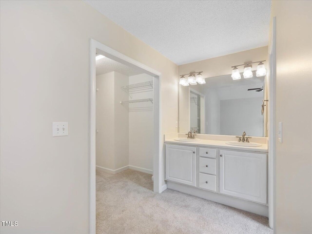full bath with double vanity, a textured ceiling, baseboards, and a spacious closet