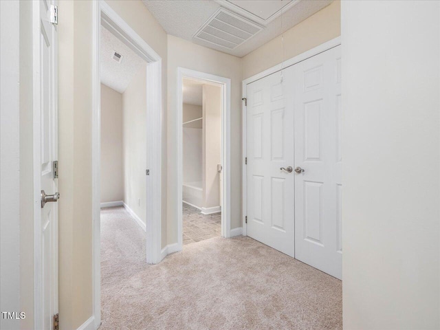 hall with carpet, attic access, and baseboards