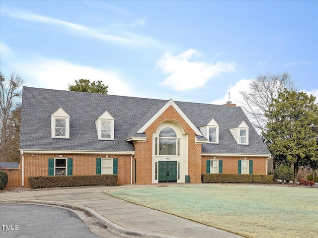 view of front of house featuring brick siding, a shingled roof, a front lawn, and a chimney