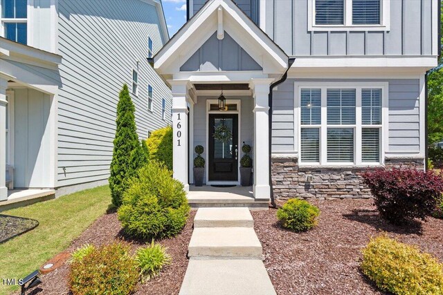 property entrance with board and batten siding, covered porch, and stone siding