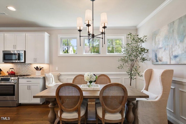 dining space with dark wood-style floors, a notable chandelier, ornamental molding, and a wainscoted wall