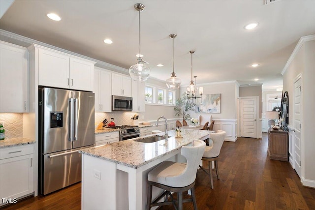 kitchen with a kitchen bar, crown molding, a sink, stainless steel appliances, and white cabinetry