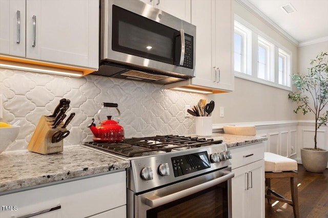 kitchen with light stone countertops, stainless steel appliances, white cabinetry, visible vents, and ornamental molding