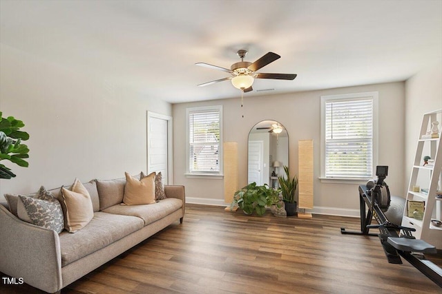 living area featuring arched walkways, ceiling fan, baseboards, and wood finished floors
