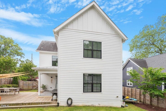 rear view of property with fence private yard, board and batten siding, a wooden deck, and a lawn