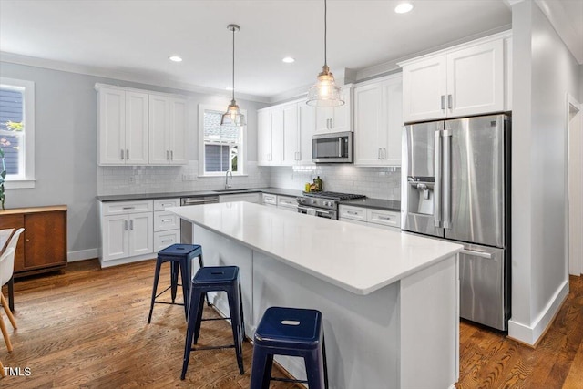 kitchen featuring a breakfast bar, stainless steel appliances, dark wood-style flooring, a sink, and white cabinetry