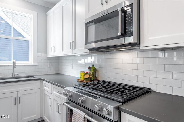 kitchen featuring white cabinets, a sink, appliances with stainless steel finishes, dark countertops, and backsplash