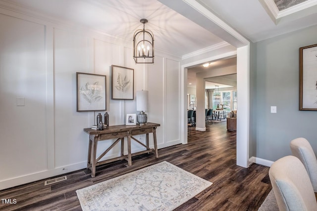 foyer with crown molding, visible vents, an inviting chandelier, dark wood finished floors, and a decorative wall