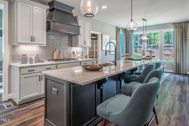 kitchen featuring premium range hood, a sink, white cabinets, and a center island with sink
