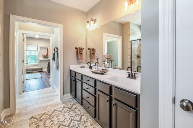 full bath featuring baseboards, a stall shower, double vanity, and a sink