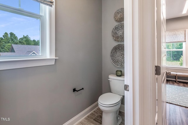 bathroom with toilet, baseboards, wood finished floors, and a healthy amount of sunlight